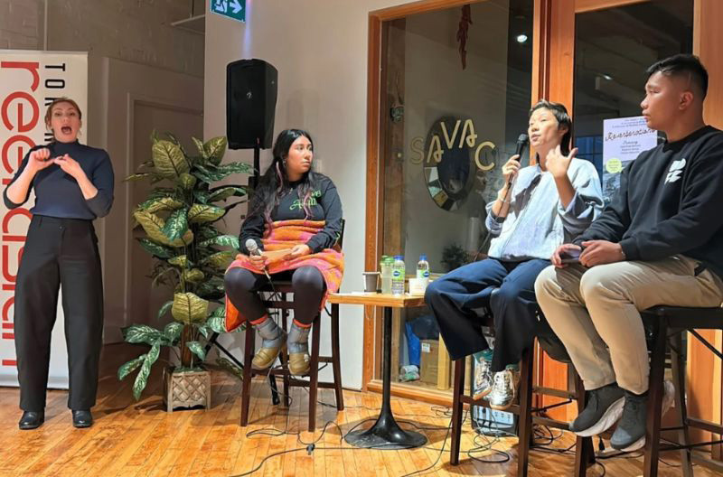 Sarah Barzak, Winnie Luk, and Clarence Cansicio seated on stools, speaking into microphones, while an ASL interpreter stands to the side; a Reel Asian banner is partially visible.